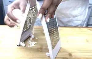 Person grating cheese on a wooden board with a stainless steel grater.